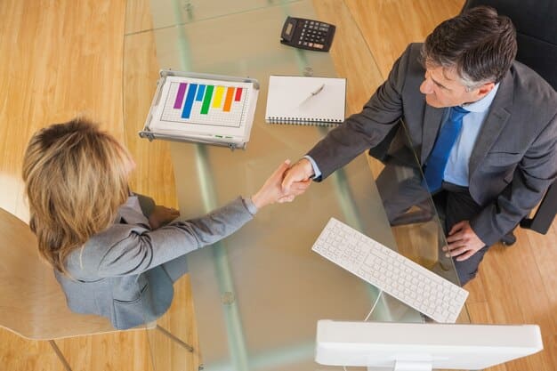 A handshake between two business figures over a table filled with legal documents and a laptop displaying financial charts, symbolizing a successful investment deal closure.
