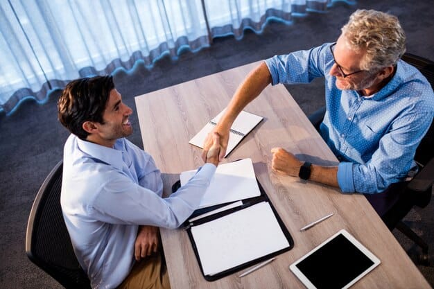 Two individuals, a startup founder and an investor, shaking hands over a table with a stack of documents and a digital tablet, symbolizing a successful partnership and agreement.