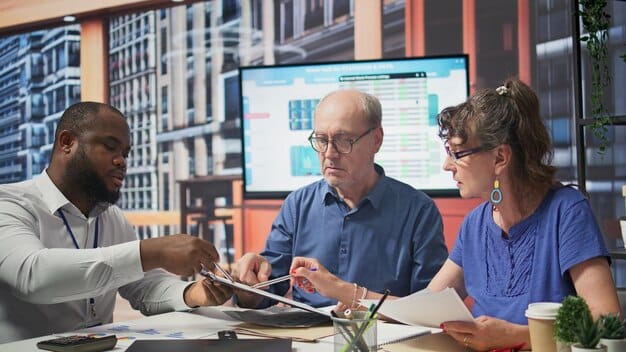 A diverse group of startup founders in a modern office collaborating around a table, with charts and data projections on a screen, symbolizing strategic planning and fundraising challenges.